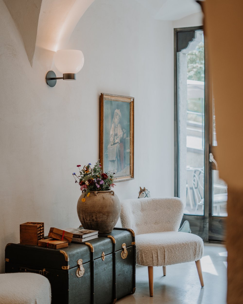 Angolo accogliente con poltrona, baule antico e vaso di fiori in stanza luminosa