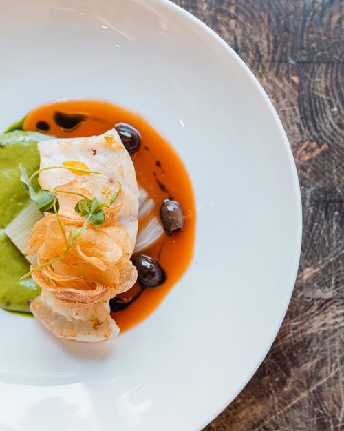 Piatto di pesce decorato con salse verde e rossa su piatto bianco