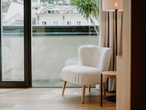 Sedia chiara accanto a lampada da terra e grande finestra con vista sugli edifici