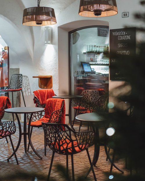 Area esterna vuota di un bar con tavoli, sedie e coperte rosse sotto lampade