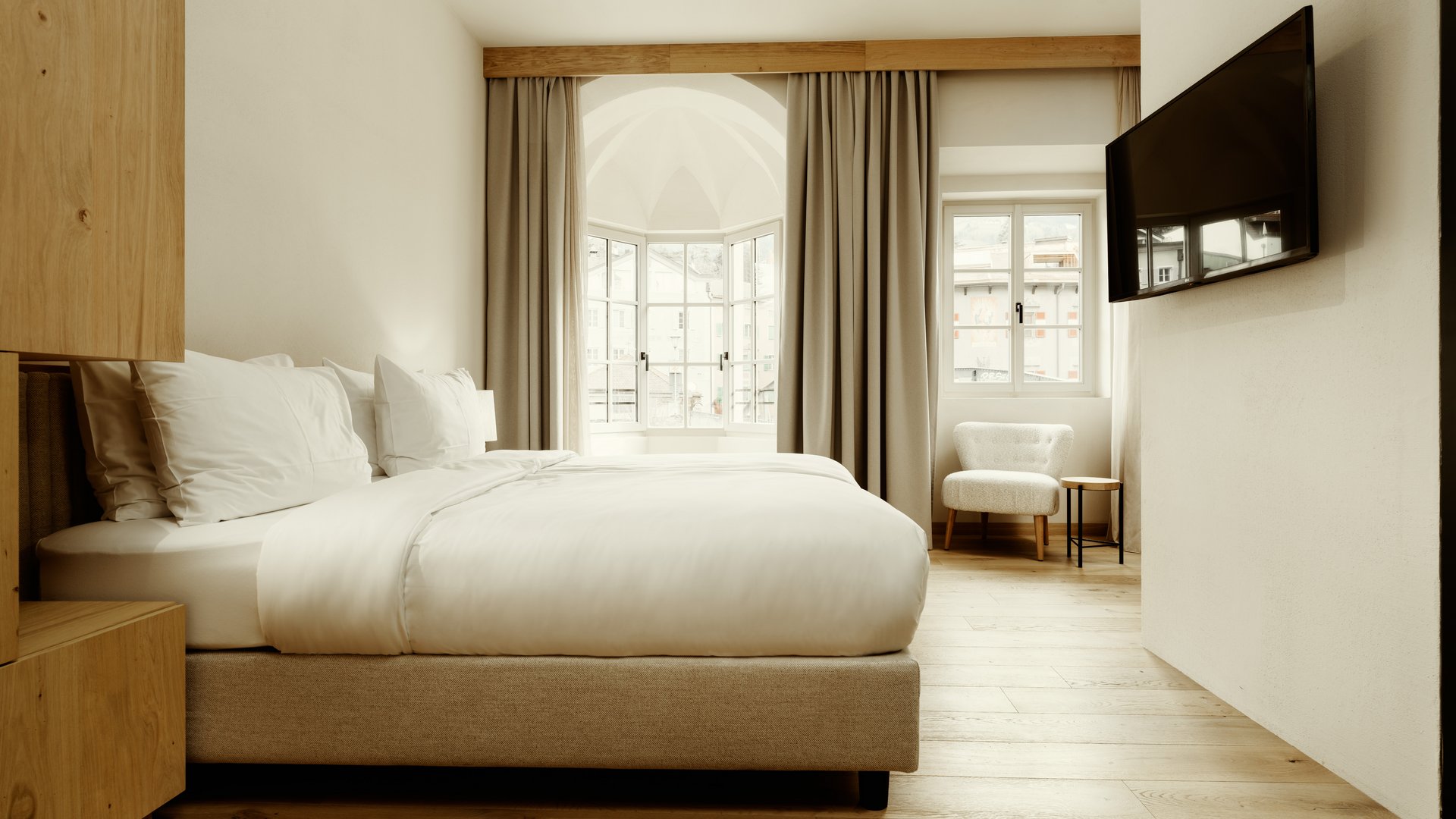 Camera d'hotel moderna con letto grande, poltrona e TV a parete