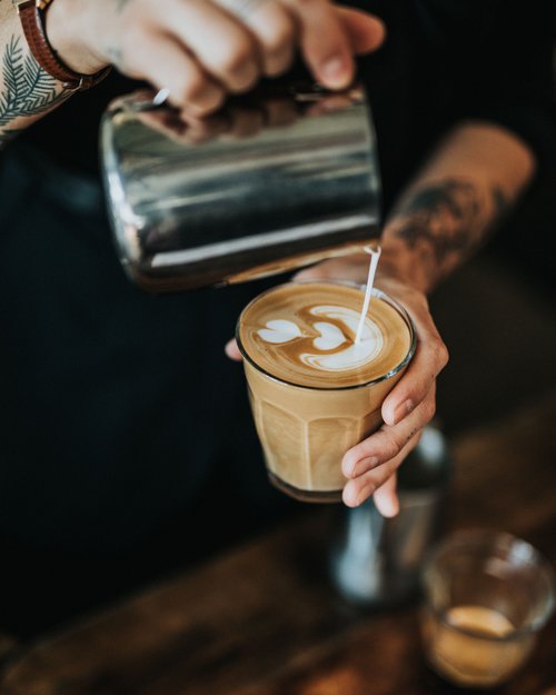 Barista versa latte nel caffè con arte del latte a forma di cuore