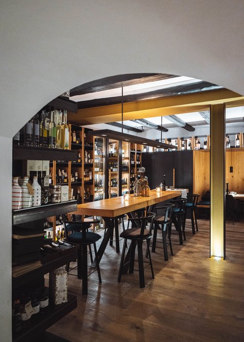 Area bar accogliente con bancone in legno, sedie e scaffali pieni di bottiglie